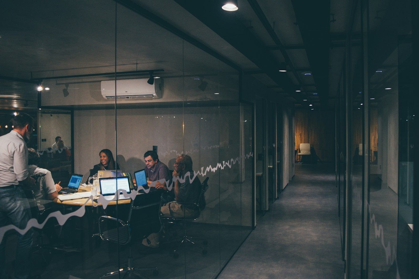 A team working late in a glazed meeting room seen from the corridor