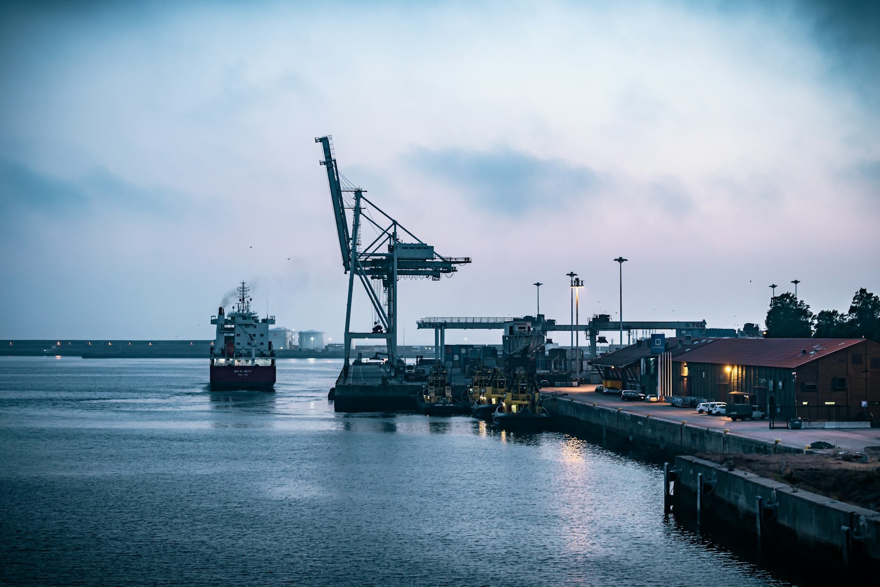 A cargo ship leaving a working port at dawn