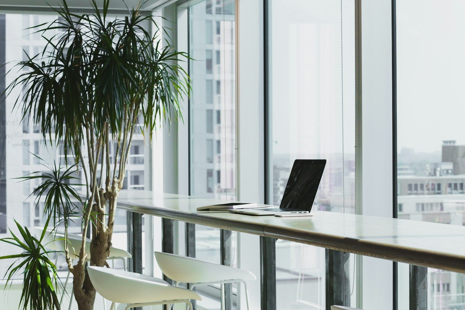A laptop on a bench desk at a window overlooking the city